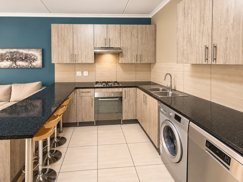 Modern open-plan kitchen featuring wood-finish cabinetry, granite countertops, integrated gas hob, oven, and breakfast bar, seamlessly connected to the living area.