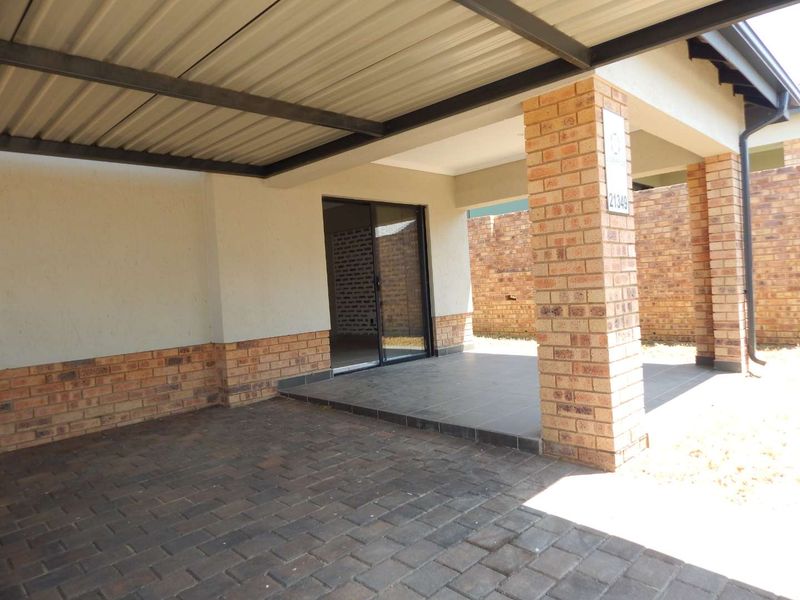 A covered patio area featuring brick pillars, paved flooring, and a sliding glass door entrance to the home.