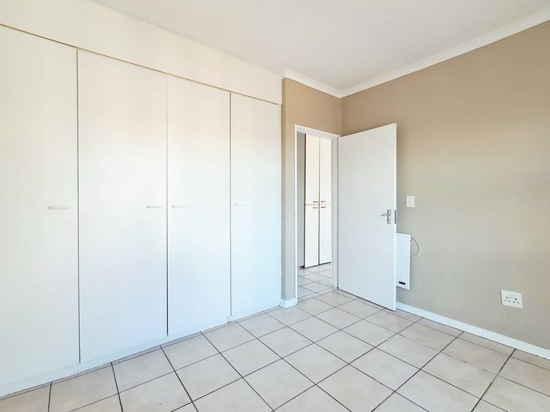 A clean, empty bedroom featuring neutral wall tones, tiled flooring, and ample built-in cupboard storage space.