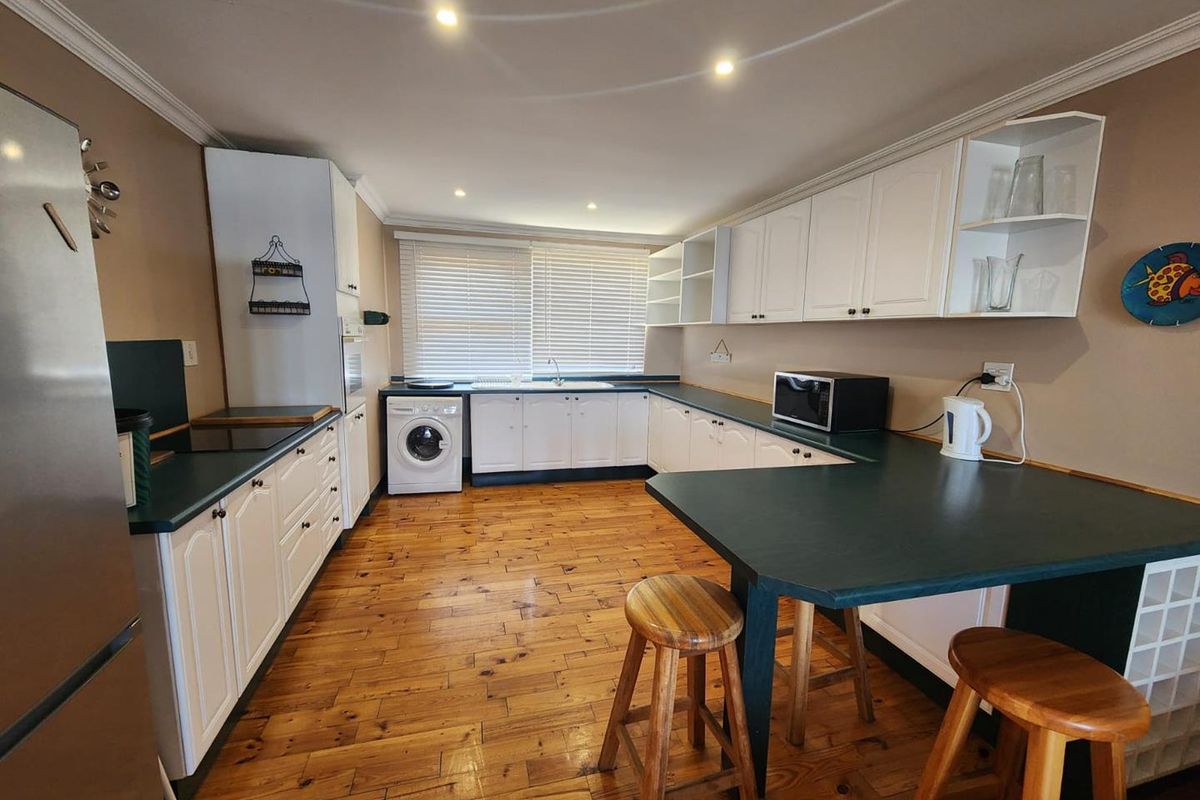 A functional kitchen featuring white cabinetry, dark countertops, timber flooring, and an integrated washing machine with a breakfast bar area.