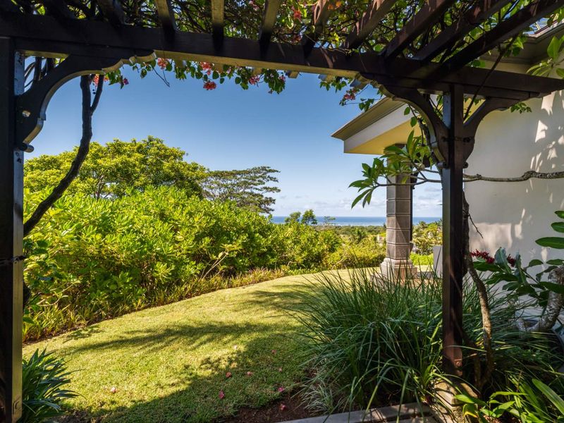 A scenic view of the lush garden and distant ocean horizon, framed by a decorative timber pergola structure.
