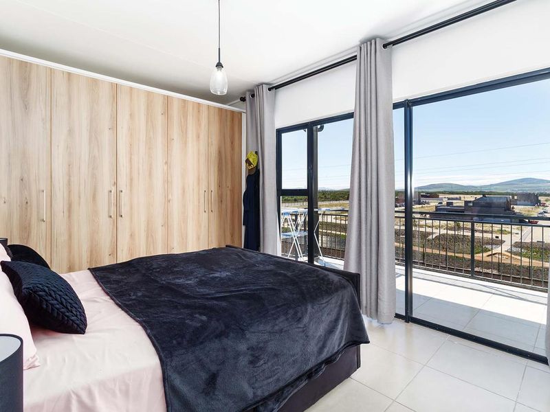 A bright bedroom featuring modern wood-finish built-in cupboards, tiled floors, and large sliding glass doors that open onto a balcony with scenic views.