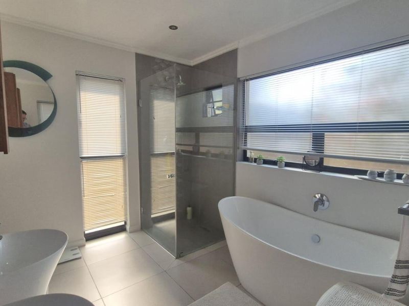 Modern bathroom featuring a freestanding bathtub, a glass-enclosed shower, tiled flooring, and large windows with fitted blinds.