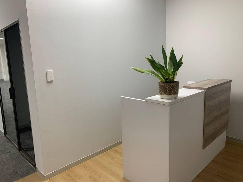 A clean and modern office reception area featuring a built-in desk and light wood-look laminate flooring.