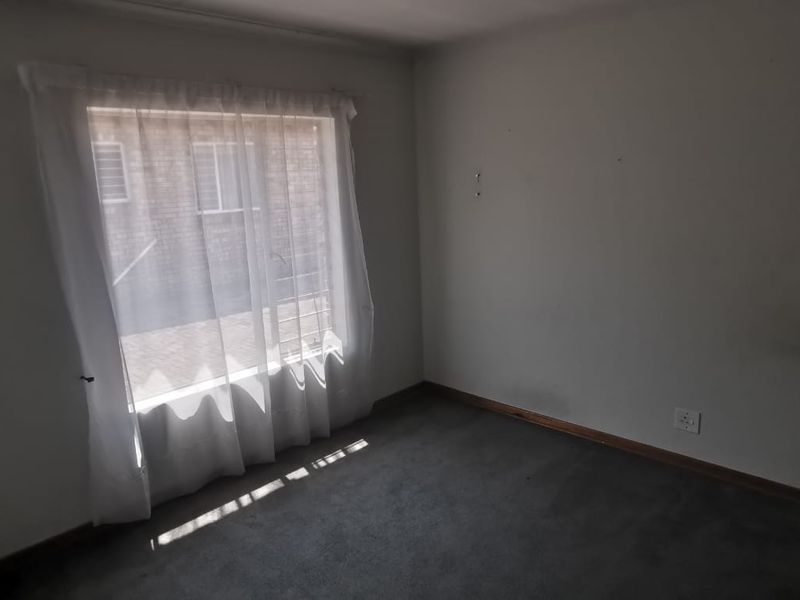 A vacant bedroom featuring carpeted flooring, a window with security bars, and neutral wall finishes, ready for personalization.