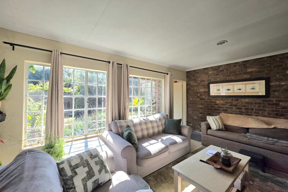 A cozy living room featuring an exposed brick accent wall and large windows that provide ample natural light and garden views.