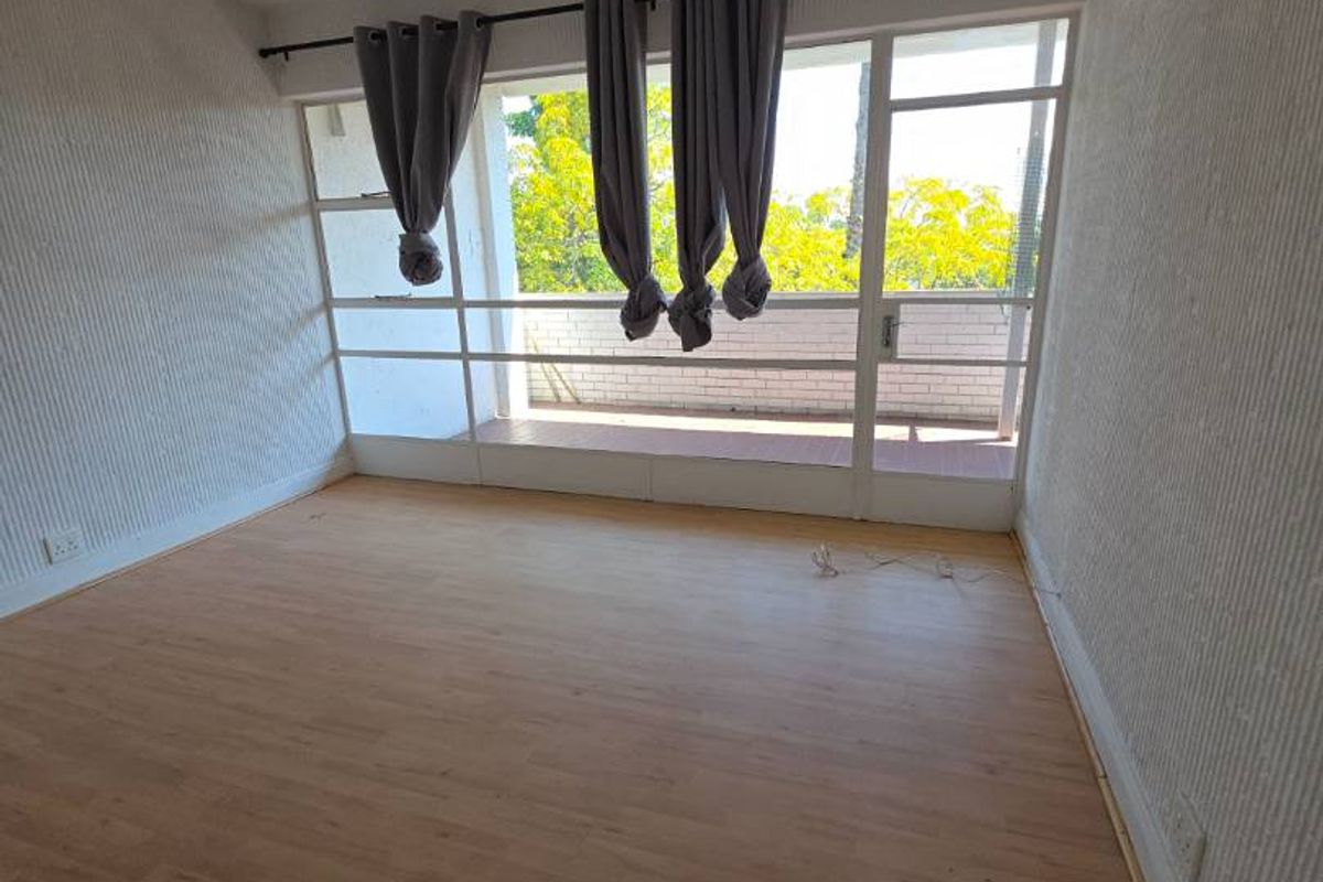 A bright, empty bedroom featuring laminate flooring, textured walls, and direct access to a private balcony through large sliding glass doors.