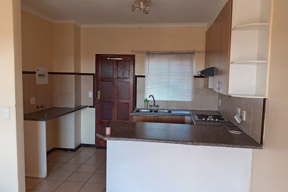 A functional kitchen featuring a breakfast bar, built-in hob, extractor fan, double sink, and ample cabinetry with tiled flooring.