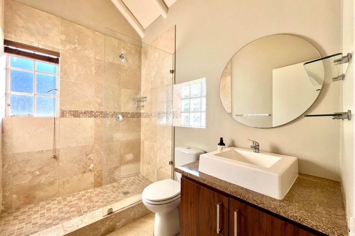 Modern bathroom featuring a walk-in shower with travertine tiling, a vanity with stone countertop, vessel sink, and a glass block window for natural light.