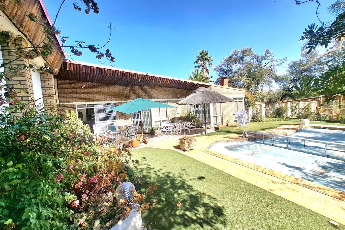 Rear exterior view featuring a swimming pool, covered patio area, and established garden with brick facade and security gates.