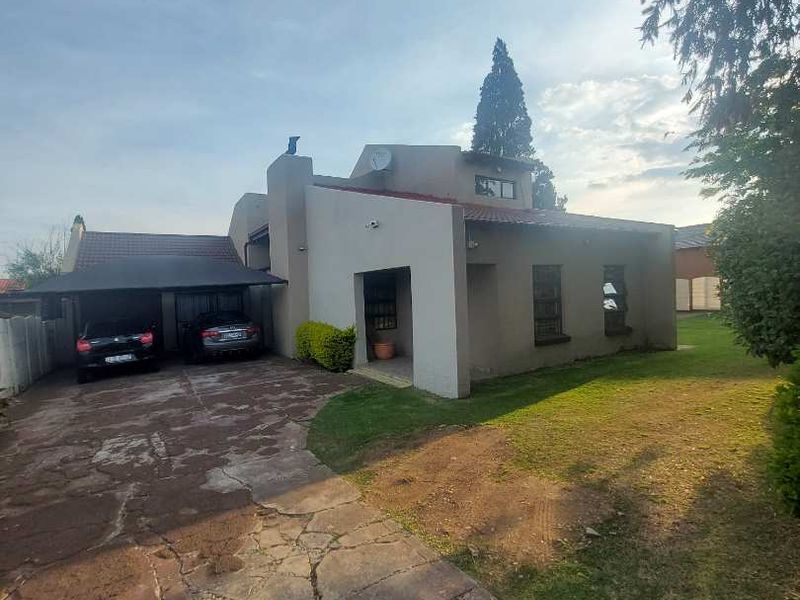Front view of the property featuring a paved driveway, carport, and established garden area.