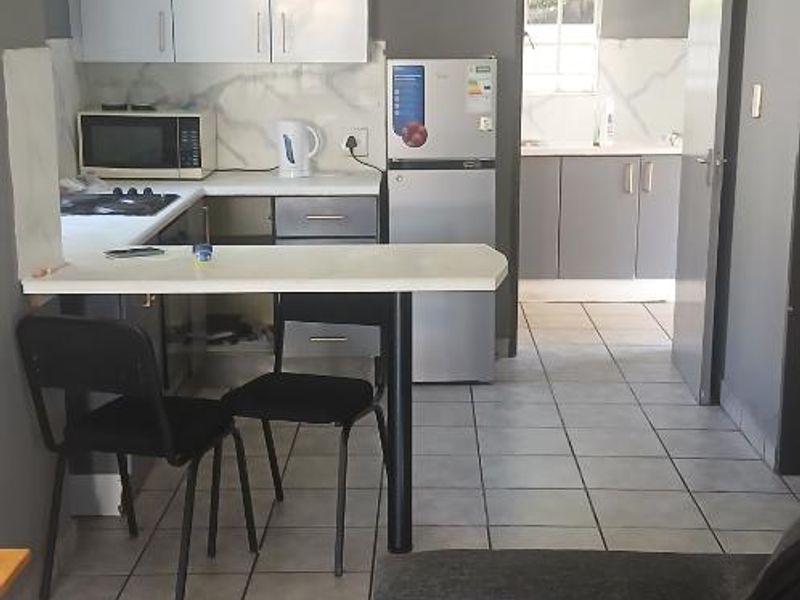 Open-plan kitchen and living area featuring tiled flooring, built-in cabinetry, and a breakfast bar, with an adjacent scullery area visible through the doorway.