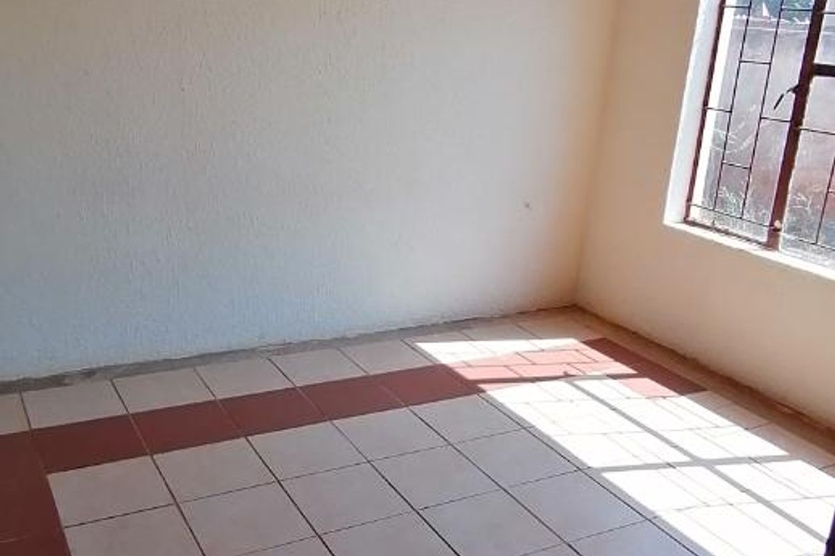 An empty bedroom featuring tiled flooring with visible incomplete tiling sections and a window fitted with security bars.