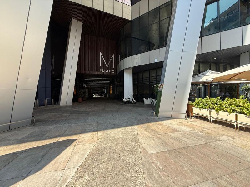 Modern commercial building entrance featuring a paved plaza, large structural columns, and contemporary glass and metal facade design.