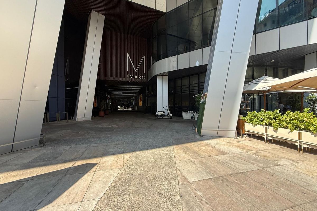 Modern commercial building entrance featuring a paved plaza, large structural columns, and contemporary glass and metal facade design.