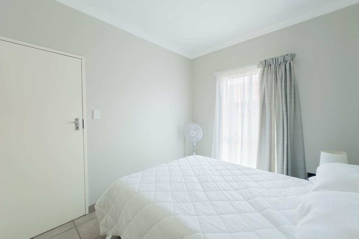 A bright and neutral bedroom featuring tiled flooring, cove cornicing, and natural light through a window with installed curtain tracks.