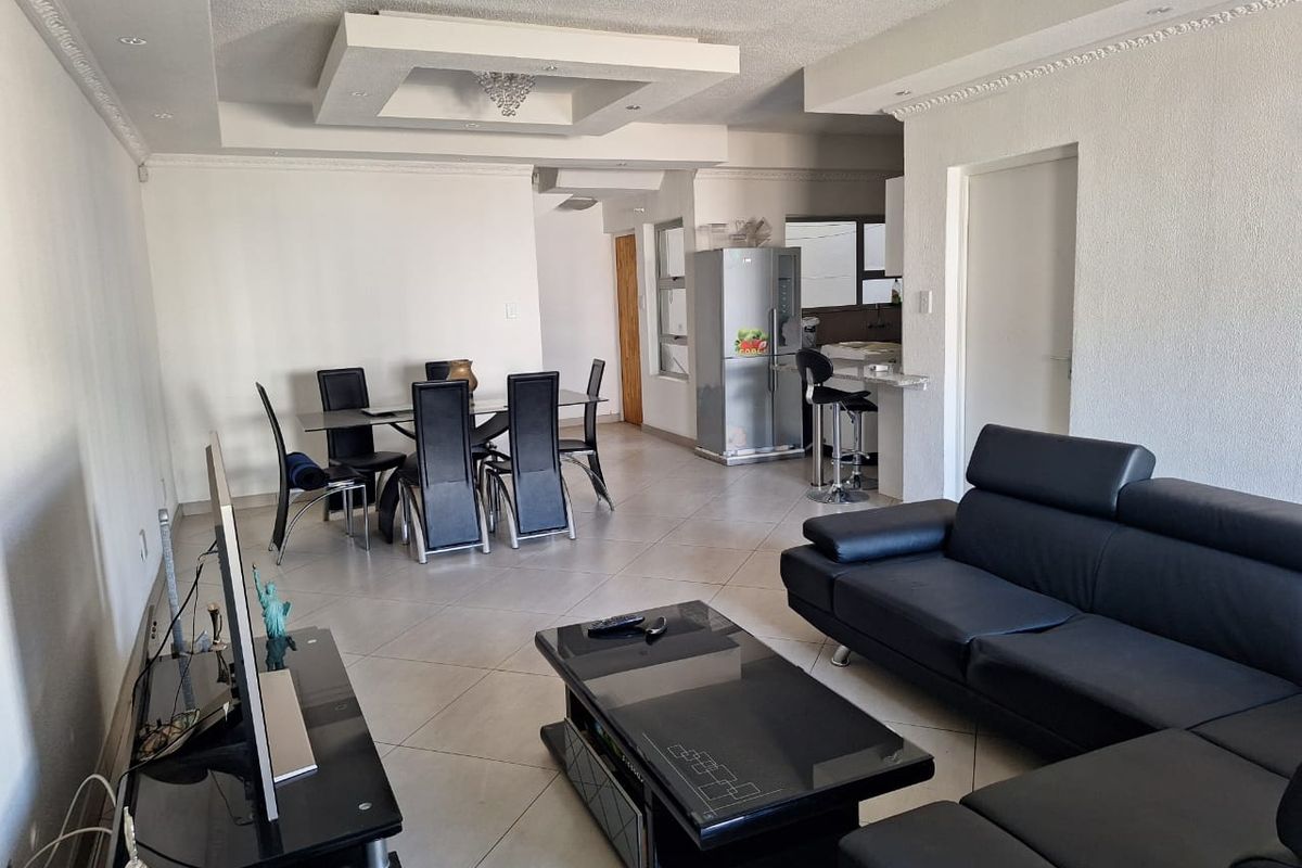 Spacious open-plan living and dining area featuring tiled flooring, recessed ceiling details, and a breakfast bar connecting to the kitchen.