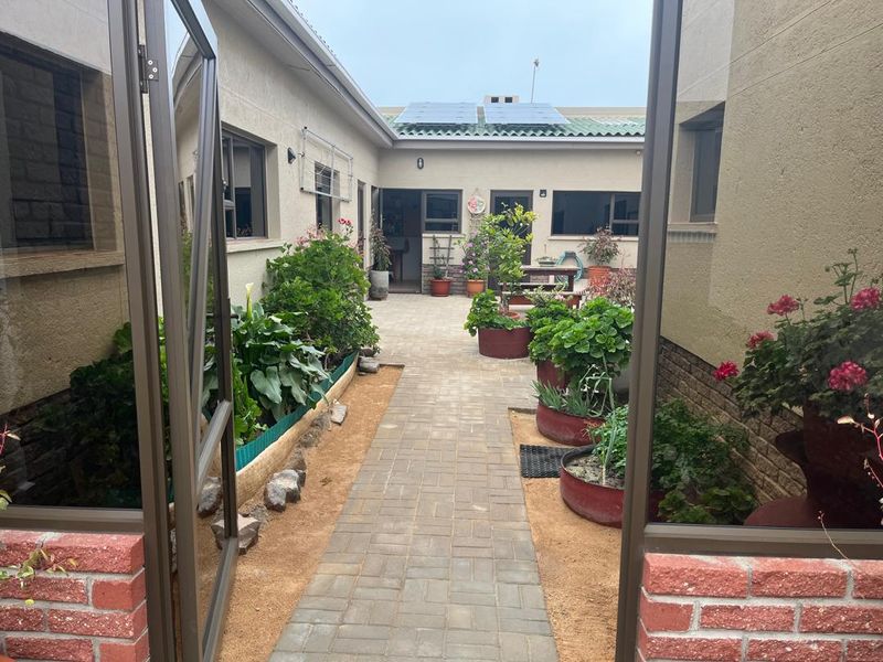 A view of a paved rear courtyard area featuring raised garden beds, brick detailing, and solar panels installed on the roof.