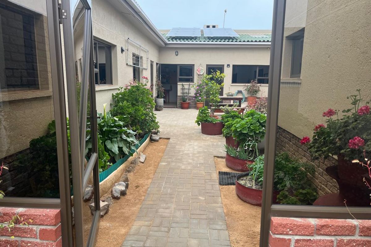 A view of a paved rear courtyard area featuring raised garden beds, brick detailing, and solar panels installed on the roof.