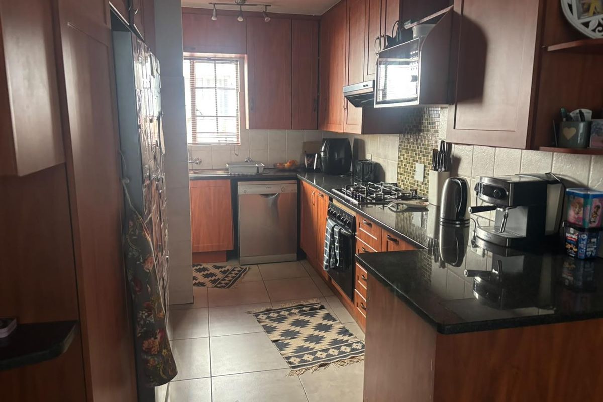 A functional kitchen featuring dark wood cabinetry, granite countertops, a gas hob, and tiled finishes, offering a classic layout with ample storage space.