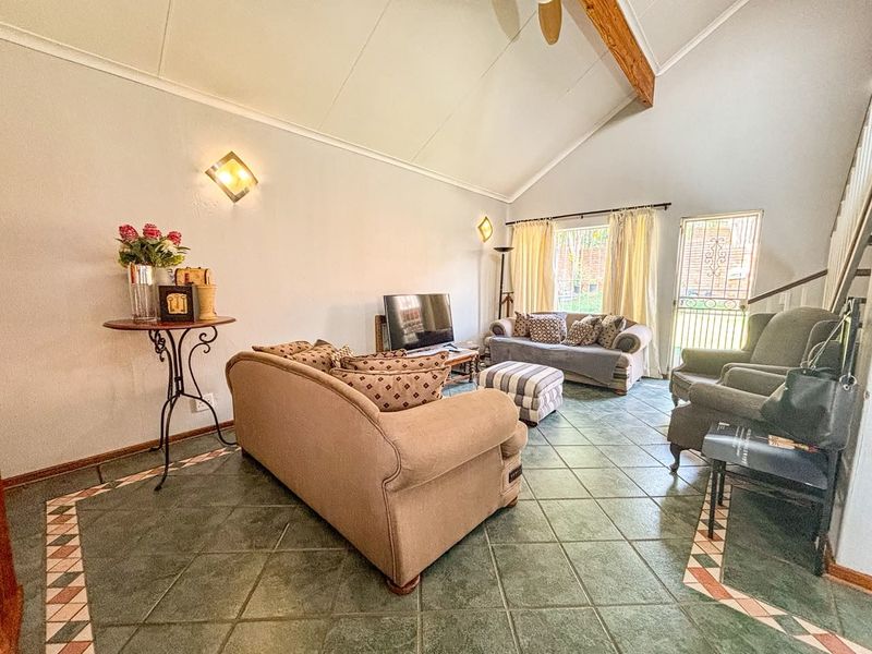 Spacious living room featuring a high vaulted ceiling with an exposed timber beam, tiled flooring, and direct access to the exterior via a security gate.