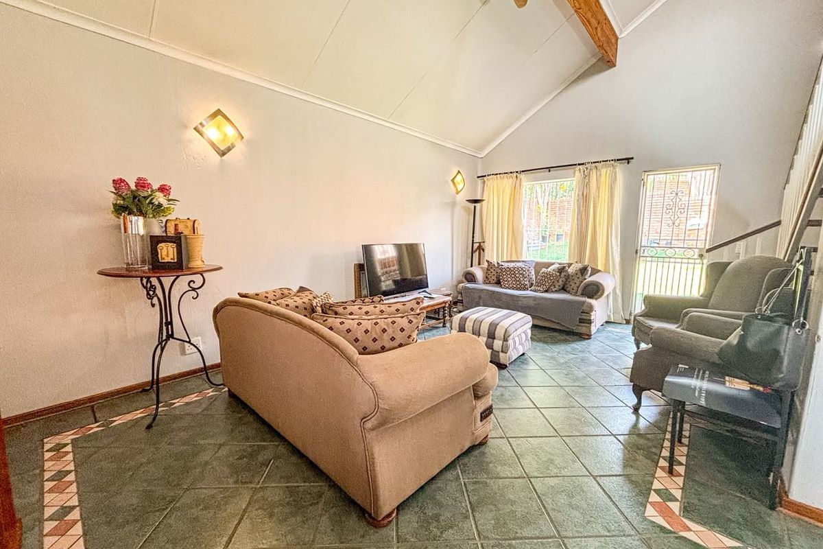 Spacious living room featuring a high vaulted ceiling with an exposed timber beam, tiled flooring, and direct access to the exterior via a security gate.
