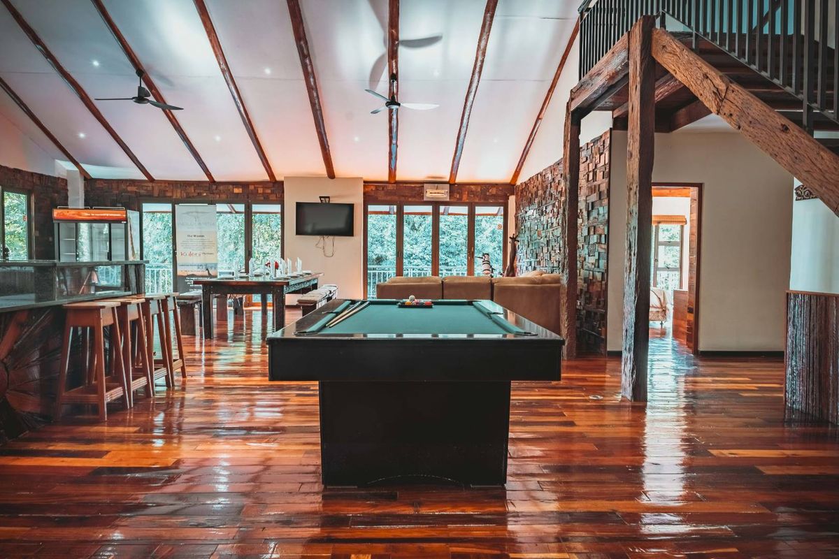 Spacious living area featuring high vaulted ceilings with exposed timber beams, rich hardwood flooring, a stone feature wall, and an integrated timber staircase.