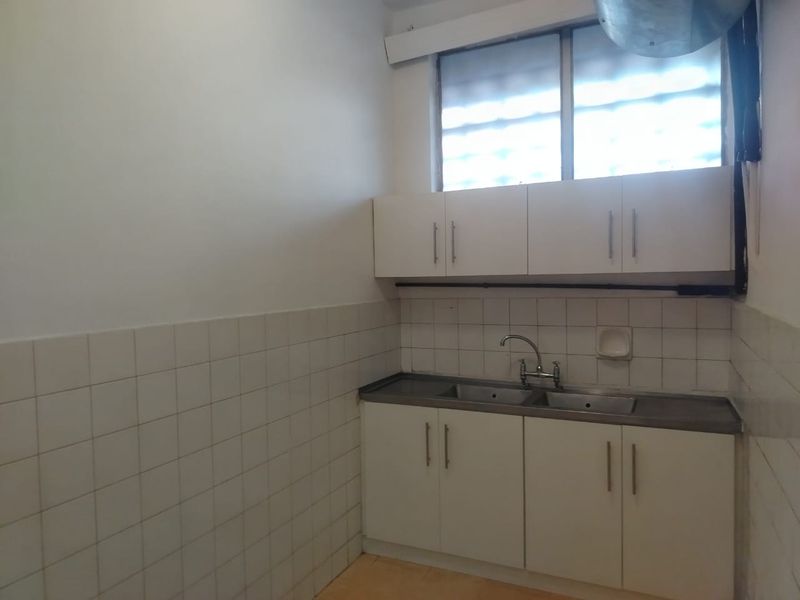 A functional, empty kitchen area featuring white cabinetry, a double bowl stainless steel sink, and tiled splashbacks, ready for modernization.