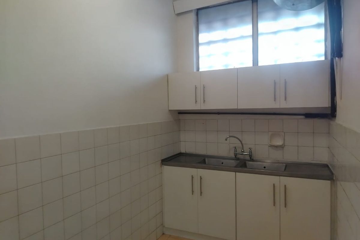 A functional, empty kitchen area featuring white cabinetry, a double bowl stainless steel sink, and tiled splashbacks, ready for modernization.
