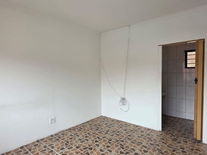 An empty bedroom featuring tiled flooring and direct access to an en-suite bathroom. The space requires minor cosmetic repairs and updates.