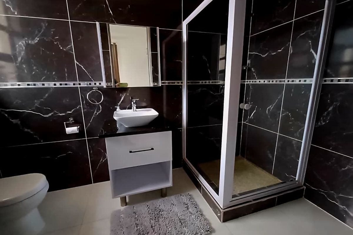 Modern bathroom featuring dark marble-effect wall tiles, a white vessel sink vanity, and a glass-enclosed shower cubicle.