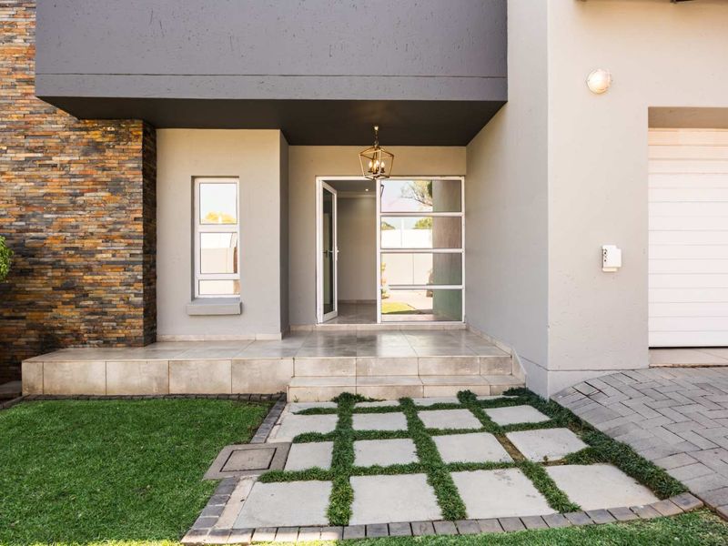Modern front entrance featuring stone cladding, a tiled porch, and a paved driveway leading to a garage.