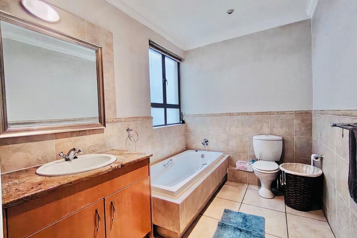 A functional bathroom featuring a built-in bathtub, vanity cabinet with granite countertop, and neutral wall tiling.