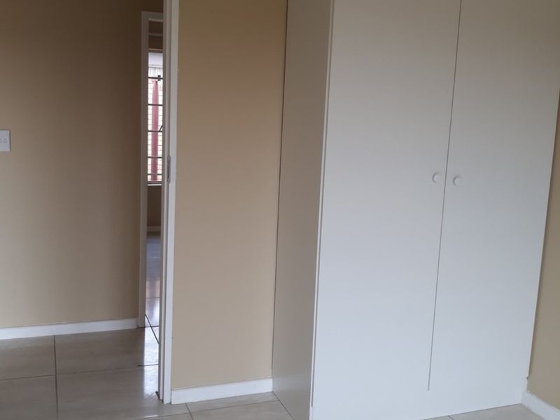 A simple bedroom featuring neutral wall paint, tiled flooring, and a built-in white wardrobe, offering a clean and functional space.