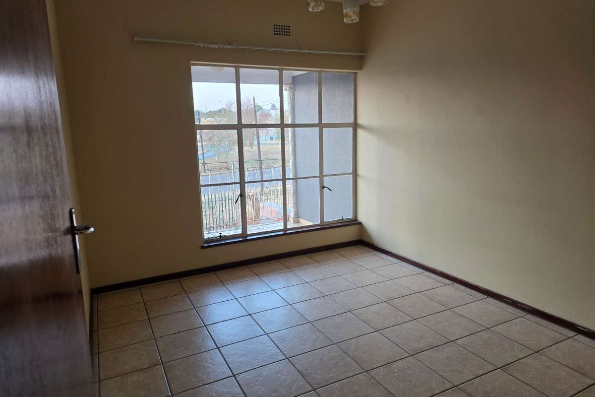 A vacant bedroom featuring tiled flooring, a large grid-style window, and a ceiling-mounted light fixture.