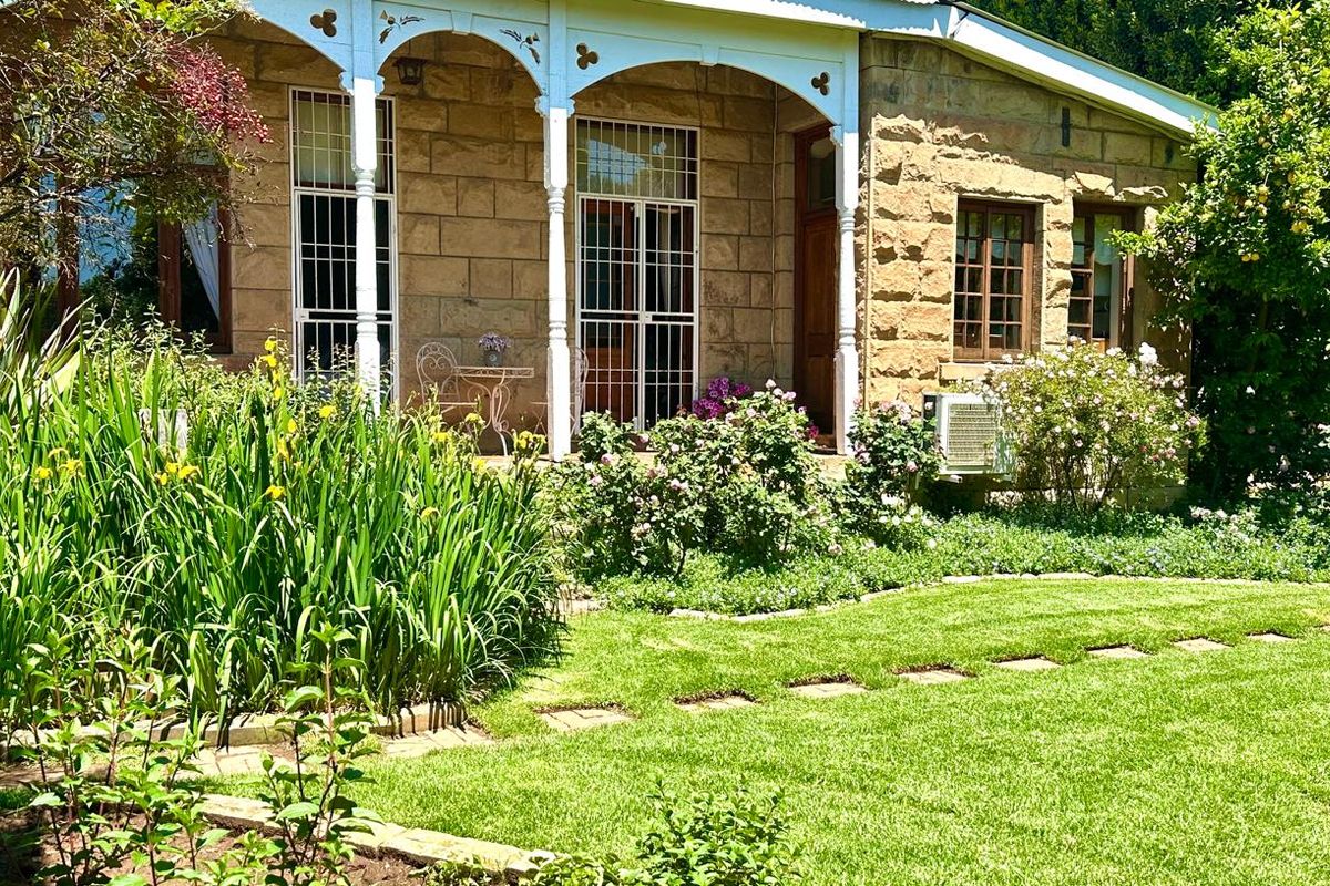 A charming sandstone house featuring a covered veranda with decorative timber fretwork, overlooking a well-maintained garden with established landscaping.