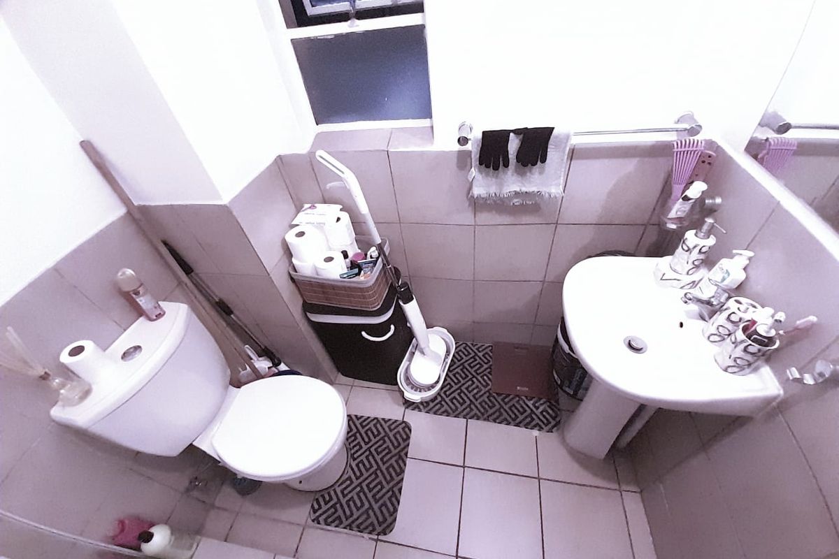 A compact bathroom featuring a pedestal sink, a standard toilet, and neutral wall and floor tiling.