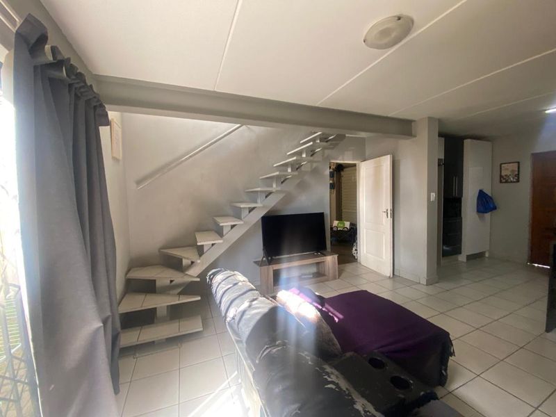 Open plan living area featuring tiled flooring, a modern staircase, and integrated storage, providing a functional and versatile space.