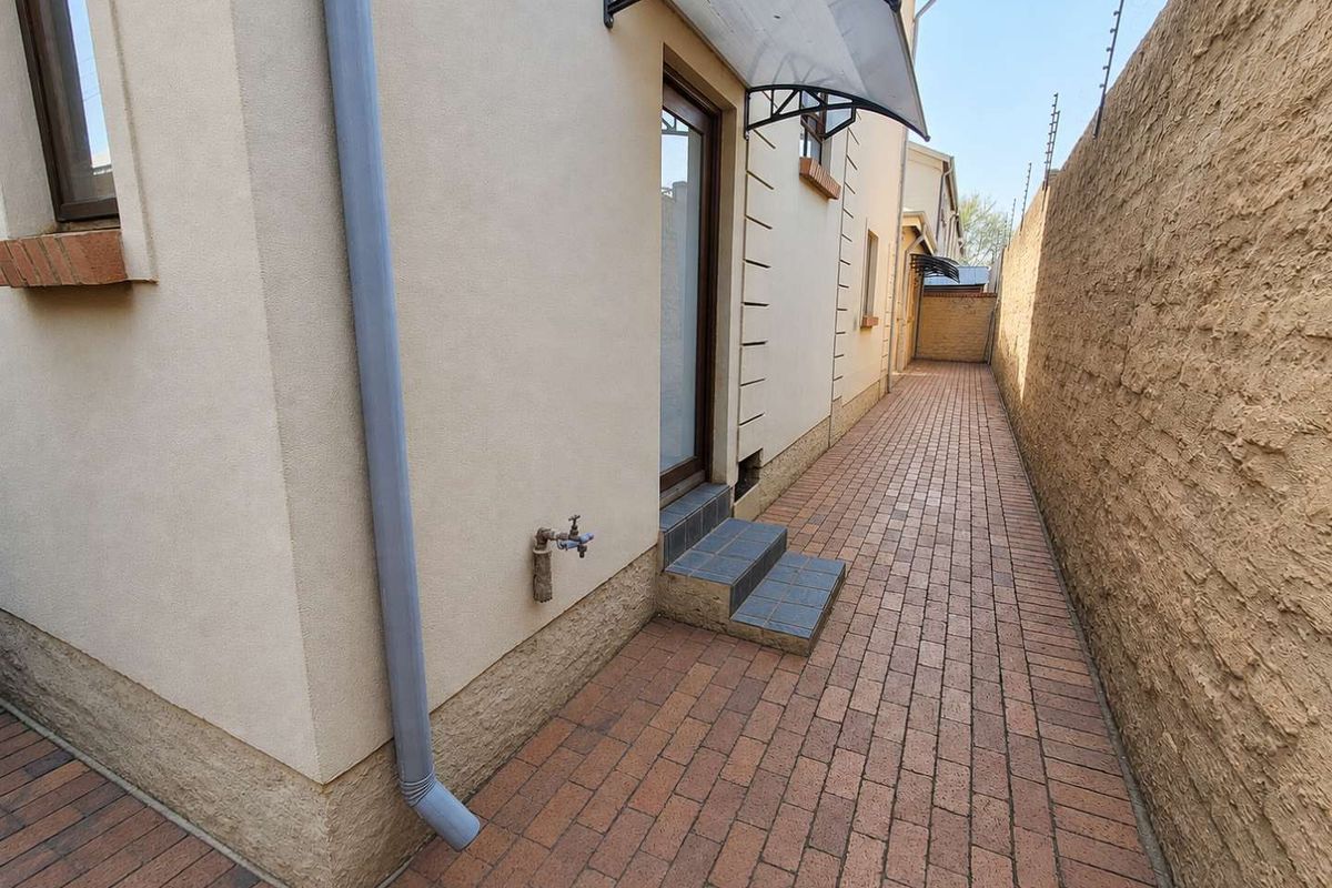 A narrow paved side passage featuring an external tap, downpipe, and a protective awning over the doorway, enclosed by a high boundary wall.