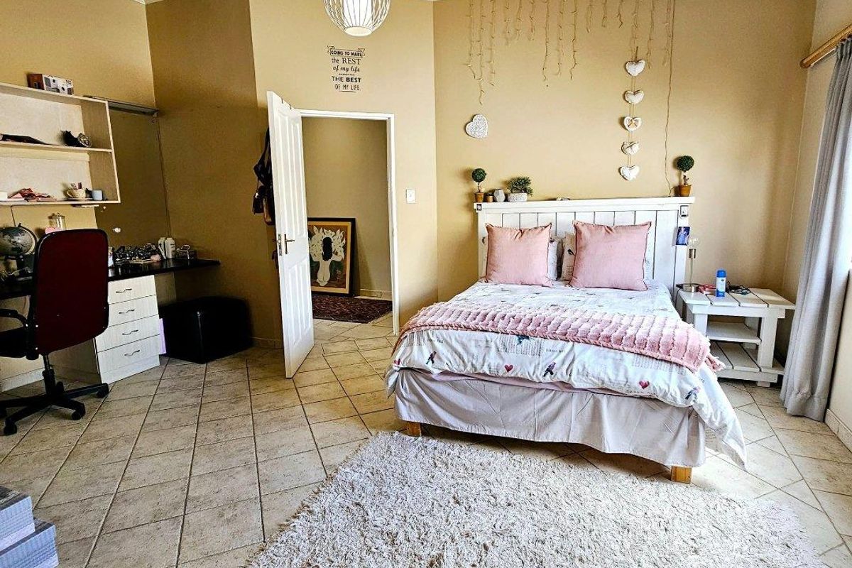 A spacious bedroom featuring tiled flooring, coved ceilings, and a built-in desk with integrated shelving units.