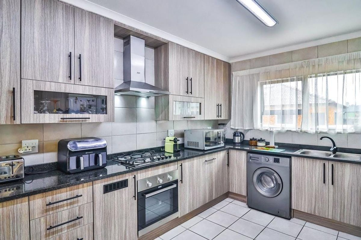 A functional kitchen featuring wood-look laminate cabinetry, granite countertops, a gas hob, built-in oven, and tiled flooring with integrated laundry plumbing.