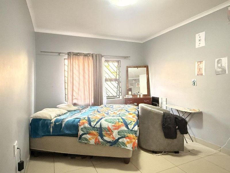 A functional bedroom featuring tiled flooring, security bars on the window, and neutral wall finishes.