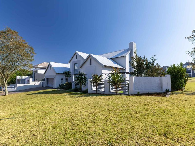 A well-maintained modern house exterior featuring a metal roof, chimney, attached garage, and a landscaped front lawn with a boundary wall.