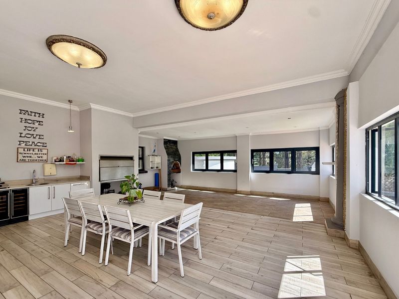 Spacious open-plan living and dining area featuring a built-in braai, pizza oven, integrated wine cooler, and modern tiled flooring with abundant natural light.