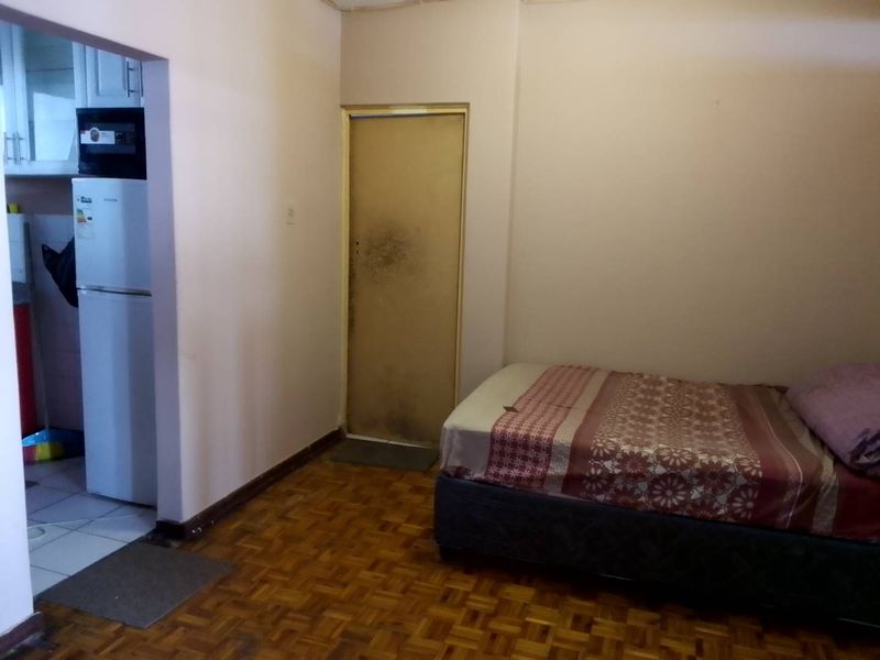 A bedroom featuring parquet flooring and an internal door, with an adjacent view into a kitchen area.