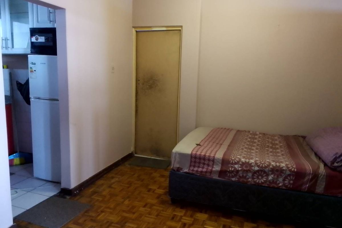 A bedroom featuring parquet flooring and an internal door, with an adjacent view into a kitchen area.