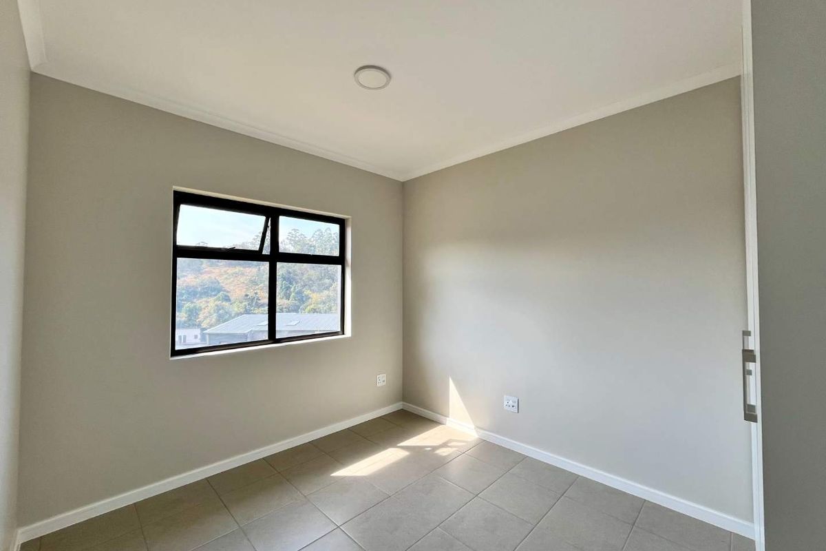 A bright, empty bedroom featuring neutral wall tones, tiled flooring, a built-in cupboard, and a window with a scenic view.