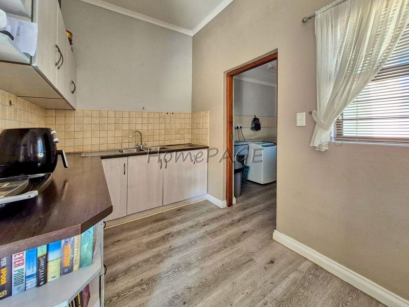 A functional scullery area featuring built-in cabinetry, a stainless steel sink, tiled backsplash, and durable laminate flooring, with an adjacent laundry room visible.