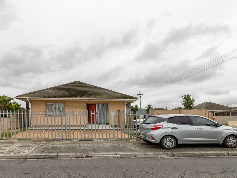 Front view of a single-story detached house featuring a tiled roof, brick exterior, and secure metal perimeter fencing with a paved driveway.