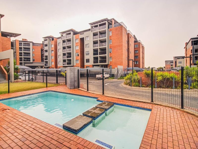 A well-maintained communal swimming pool area featuring brick paving and secure mesh fencing, set within a modern townhouse complex.